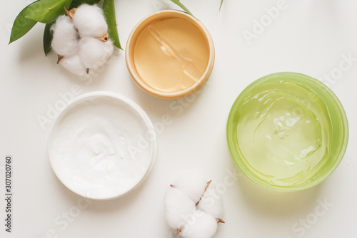 Jars of cream, aloe gel and moisturizing face patches on a white background next to cotton flowers. Nature Cosmetics for hand and face skin care, a means to reduce wrinkles on hands, moisturizing