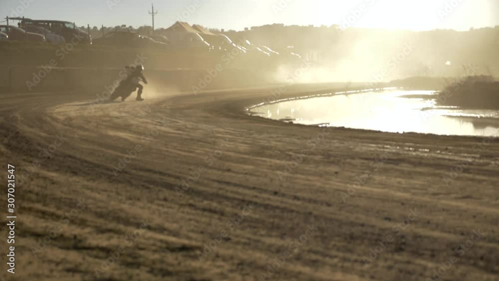 Motorcycle sportsman riding through dust dawn track in slow motion. Passing close, low to rising dolly camera angle. Motorcycle sportsman riding through dust dawn track in slow motion. Passing close, low to rising dolly camera angle.