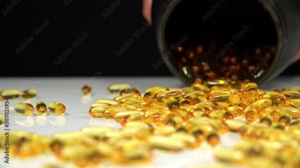 Omega 3 tablets pour out from a black can. On a black background. Omega 3 tablets pour out from a black can. On a black background.