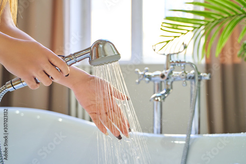 Water pours out of the shower on the girl's hands. On a blue background. Woman checks the temperature of the water in the background of the bathroom photo