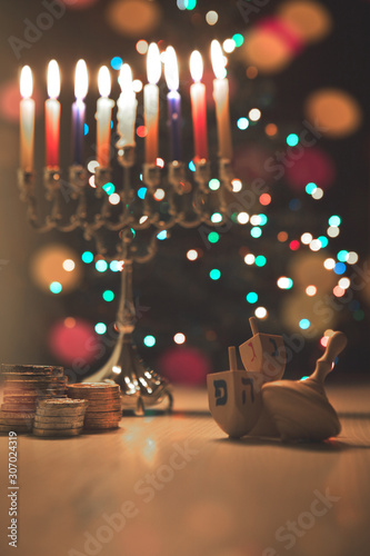 Hanukkah traditional chandelier (menorah) burning candles on the background of a Christmas tree with colorful lights.
