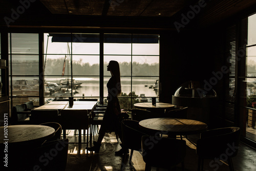 Silhouette Of A Young Stylish Girl In Sunglasses Walking Along A Panoramic Window. On the background of the yacht. Business woman © boykovi1991