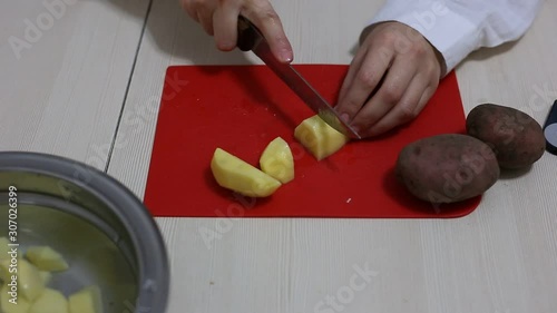 Hands cut potatoes on a red board on the table. Cooking process.