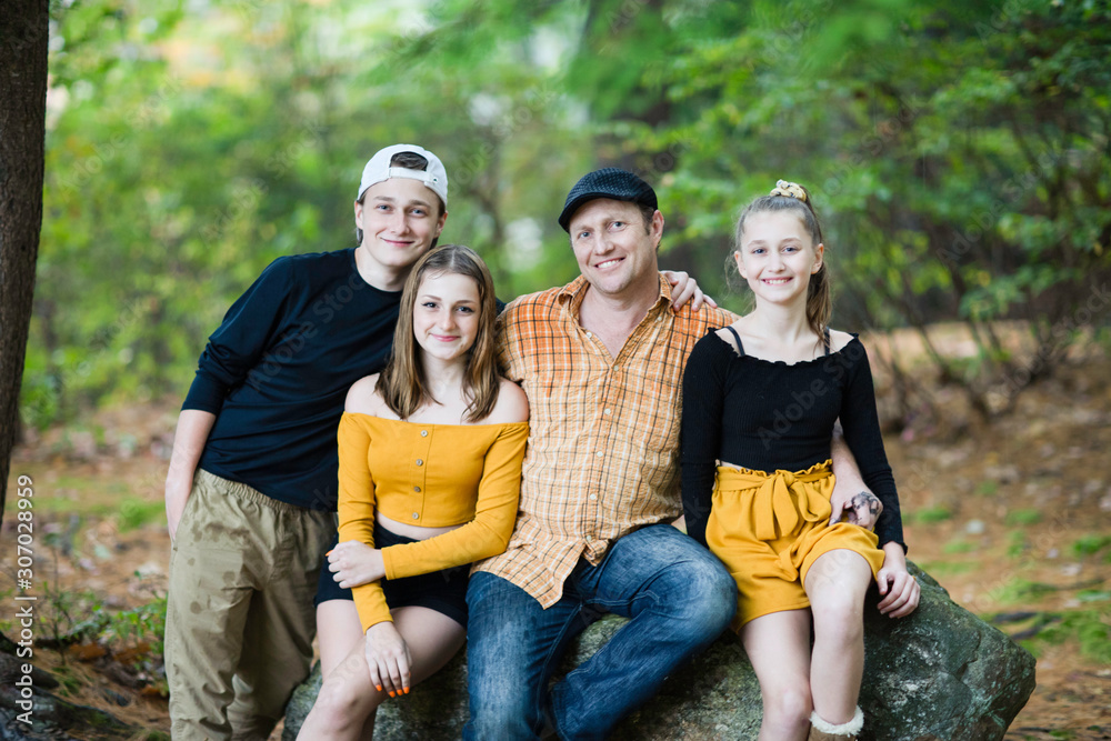 Fototapeta premium White Caucasian family father and teenager son and daughter sitting on the rock at fall forest