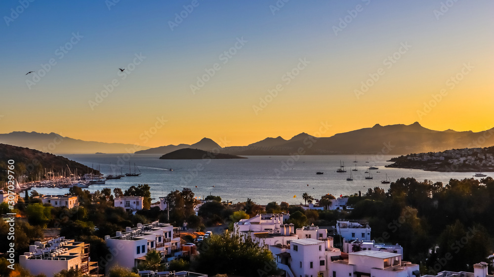 Bright colorful sunset in the beautiful bay of the Aegean sea with islands, mountains, boats and birds in the sky . Summer holiday concept and travel background