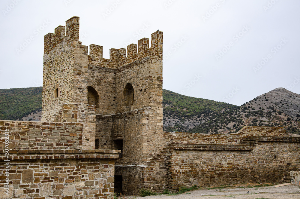 Tower and wall of an old fortress in the mountains. Ruins and excavations.