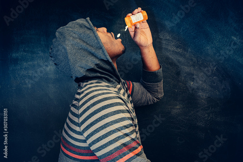 Photography african american male pouring pills into mouth wearing hooded shirt against a da