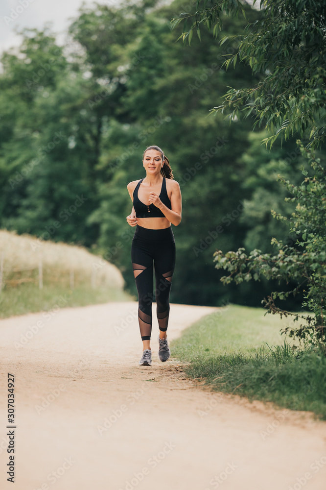 Portrait of young beautiful fit woman jogging in nature, wearing black activewear, athlete model posing outdoors, sport fashion Portrait of young beautiful fit woman jogging in nature, wearing black activewear, athlete model posing outdoors, sport fashion