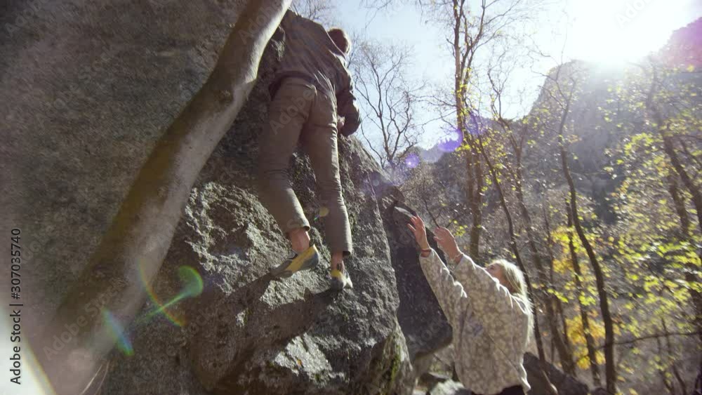 Man climbing boulder as woman holds arms up for safety as he climbs to the top. Man climbing boulder as woman holds arms up for safety as he climbs to the top.