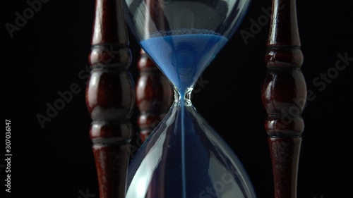 Hourglass clock time concept. Old vintage wood frame blue sand clock countdown on dark background. Close up.