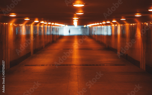 View with a shallow depth of field of a long underground pass with three rows of lamps stretching into the vanishing point with a human silhouette at the end  selective focus in the foreground