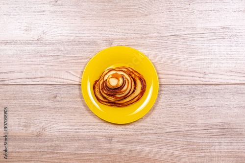 Pancakes of different sizes in a yellow plate on a wooden background top view