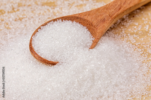 Spoon full of granulated sugar  on a wooden background