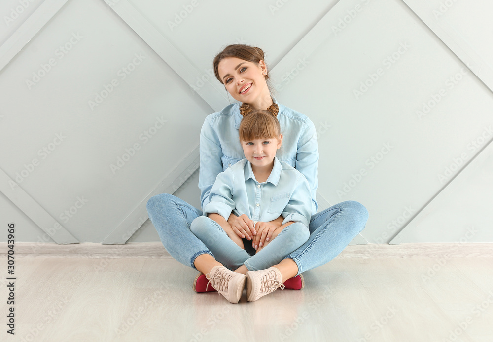 Fototapeta premium Portrait of happy mother and daughter sitting on floor near wall