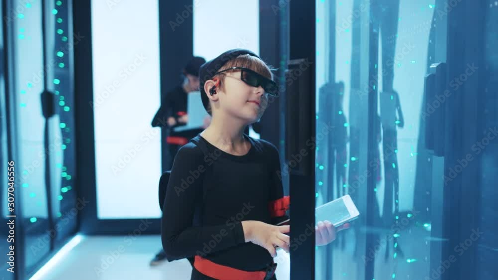 Young boy hacker opening server cabinet, copying network data into a tablet, taking part in important secret mission with friends. Spy kids. Data center cybercrime. Young boy hacker opening server cabinet, copying network data into a tablet, taking part in important secret mission with friends. Spy kids. Data center cybercrime.