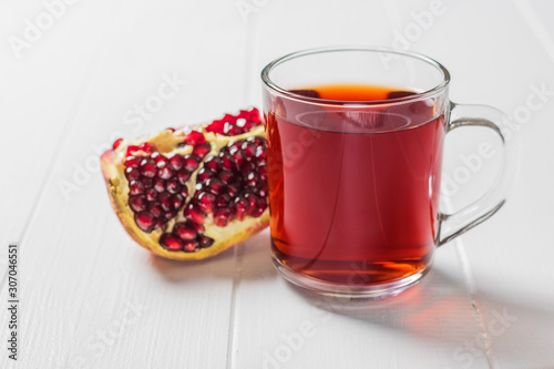 A mug of pomegranate juice and a ripe pomegranate on a white table.