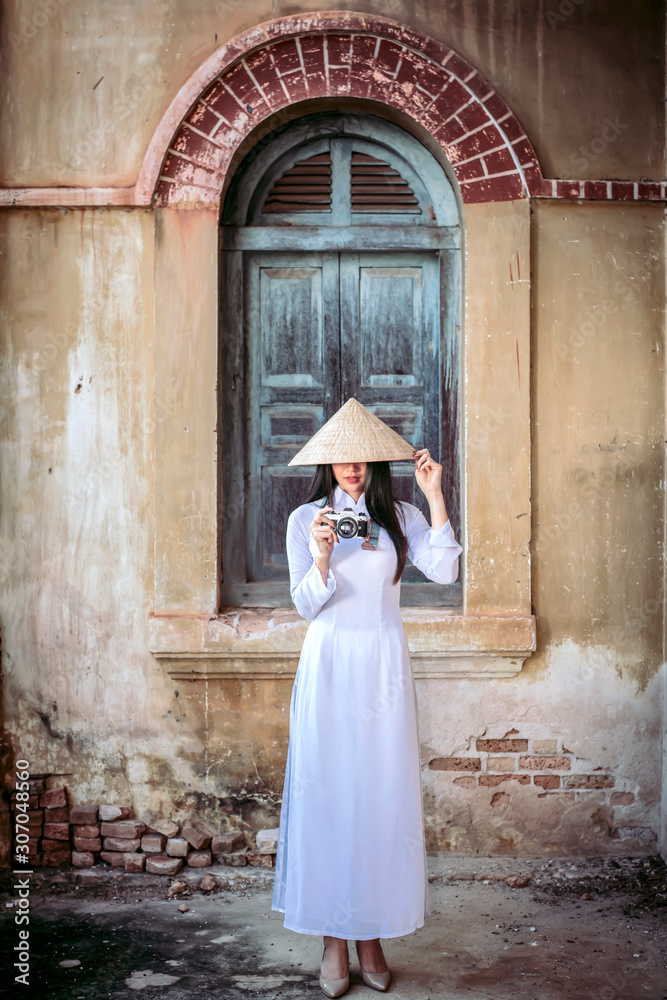 A beautiful woman in Vietnam's national costume is standing and catching a sun hat. While taking pictures