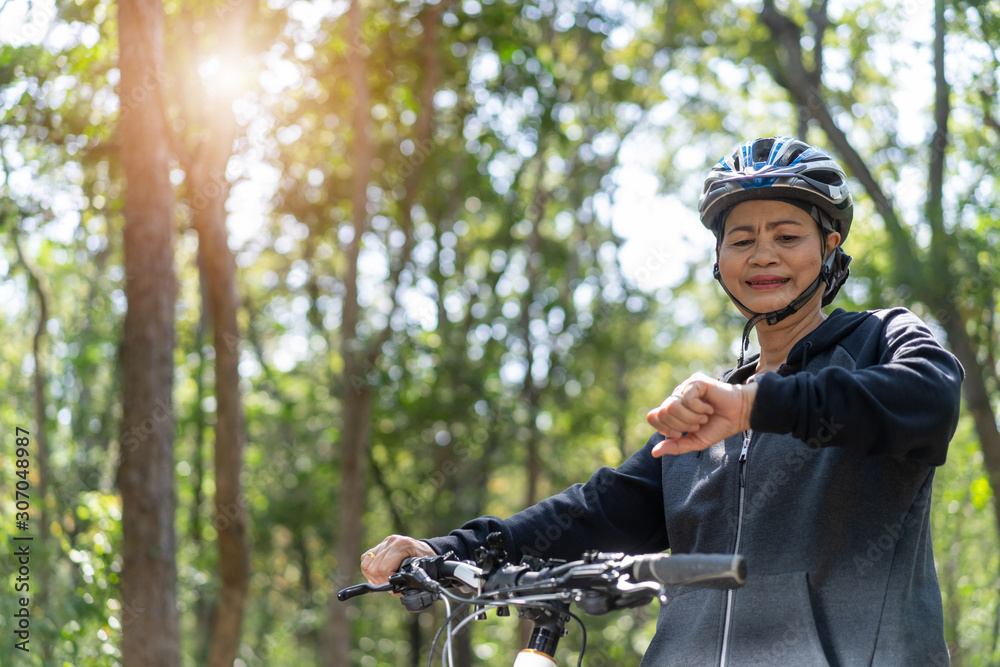 Senior asian woman bicycle in the park, With checking time or heart rate from smart watch Senior asian woman bicycle in the park, With checking time or heart rate from smart watch