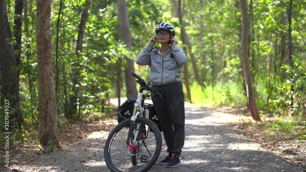 Attractive senior asian woman wearing a helmet with bicycle in park Attractive senior asian woman wearing a helmet with bicycle in park