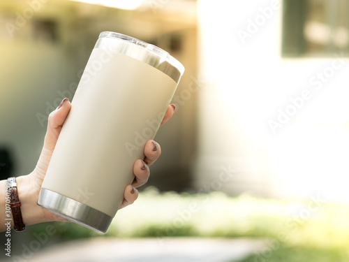 Closeup hand of a woman holding a reusable insulated stainless steel tumbler to show awareness of 'Say No to single use plastic’ and ‘Zero Waste’ in outdoor area of cafe. photo