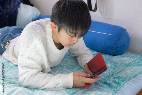 スマホを見てベッドに寝転がる男子高校生