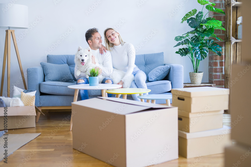 Young beautiful couple with dog sitting on the sofa at new home around cardboard boxes Young beautiful couple with dog sitting on the sofa at new home around cardboard boxes