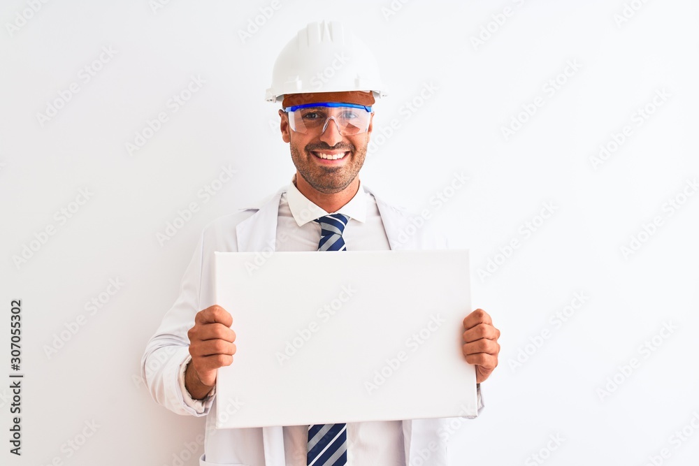 Young chemist man wearing security helmet holding signboard over isolated background with a happy face standing and smiling with a confident smile showing teeth Young chemist man wearing security helmet holding signboard over isolated background with a happy face standing and smiling with a confident smile showing teeth