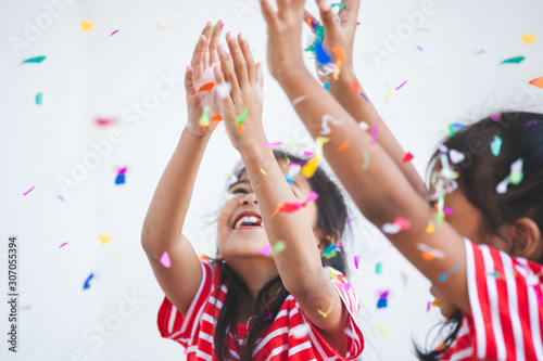 Cute asian child girl and her sister play with colorful confetti together to celebrate in their party with fun