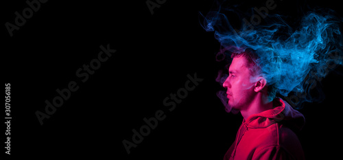 Portrait of a guy in profile face looking on a black isolated background with a feeling of sadness and loneliness, around the head a cloud of blue and pink smoke. The soul and feelings.