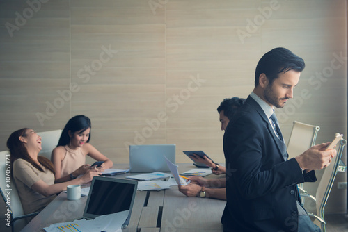 Obraz na plátne business man smart and handsome standing using smartphone with team mates workin