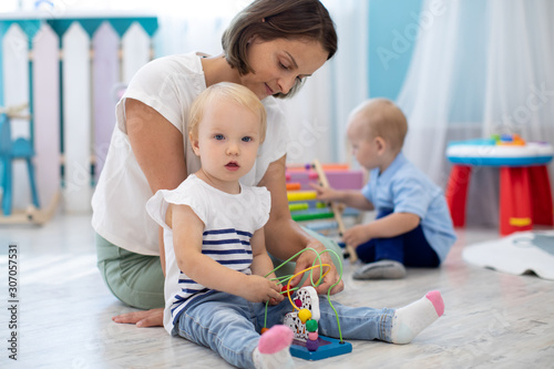 Child toddler playing with toys with teacher or babysitter indoors