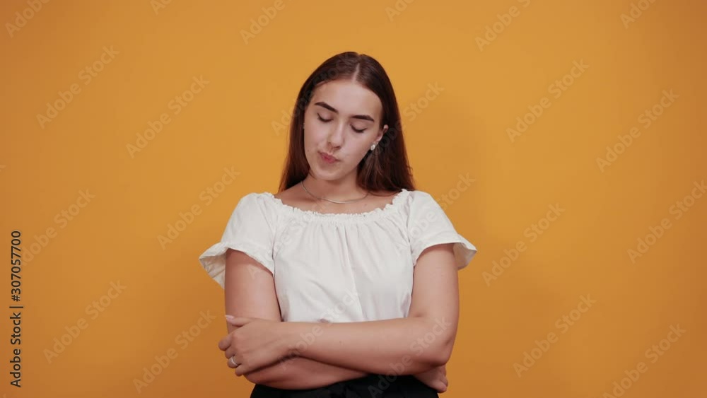 Resentful young woman blowing lips isolated on orange background in studio in casual white shirt. People sincere emotions, lifestyle concept. Resentful young woman blowing lips isolated on orange background in studio in casual white shirt. People sincere emotions, lifestyle concept.