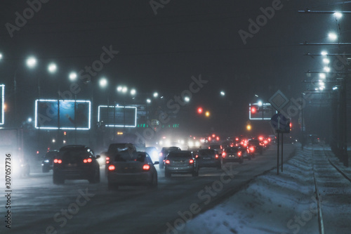 snowy winer night on a road with traffic in a city with lots of lights and billboards in the street