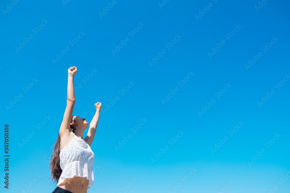 Happy woman with tanned slim body breathing fresh air raising her arms up, enjoying a sunny summer holiday on beach destination against blue sky, outdoors. Travel and well being lifestyle. Happy woman with tanned slim body breathing fresh air raising her arms up, enjoying a sunny summer holiday on beach destination against blue sky, outdoors. Travel and well being lifestyle.