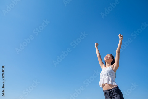 Happy woman with tanned slim body breathing fresh air raising her arms up, enjoying a sunny summer holiday on beach destination against blue sky, outdoors. Travel and well being lifestyle. © max_play