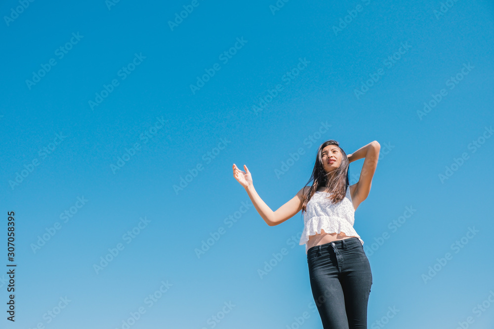 Happy woman with tanned slim body breathing fresh air raising her arms up, enjoying a sunny summer holiday on beach destination against blue sky, outdoors. Travel and well being lifestyle. Happy woman with tanned slim body breathing fresh air raising her arms up, enjoying a sunny summer holiday on beach destination against blue sky, outdoors. Travel and well being lifestyle.