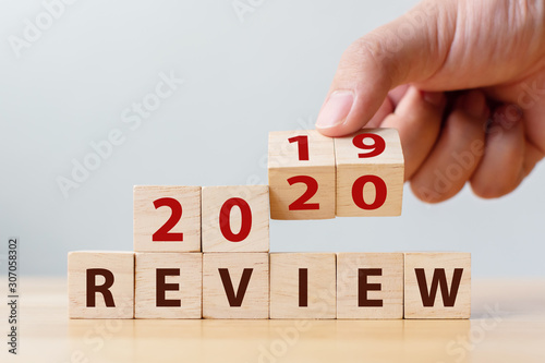 2020 review concept. Hand flip wood cube change year 2019 to 2020 and the word REVIEW on wooden block on wood table