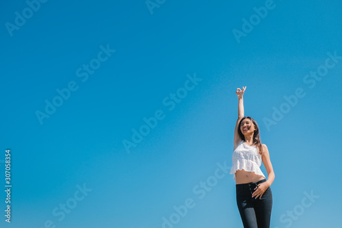 Happy woman with tanned slim body breathing fresh air raising her arms up, enjoying a sunny summer holiday on beach destination against blue sky, outdoors. Travel and well being lifestyle.