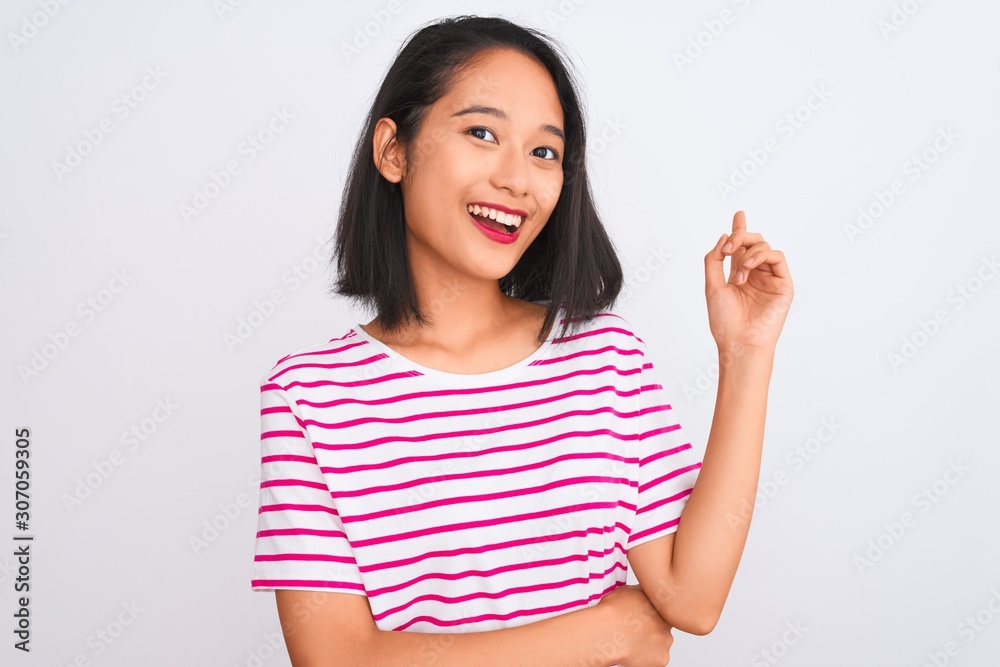 Young chinese woman wearing striped t-shirt standing over isolated white background with a big smile on face, pointing with hand and finger to the side looking at the camera.