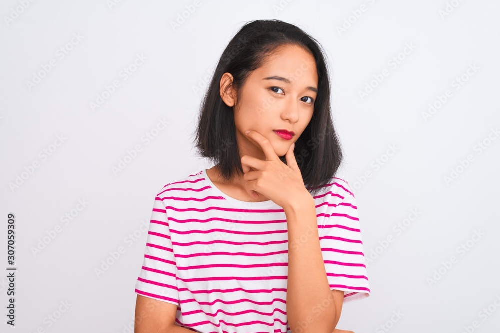 Young chinese woman wearing striped t-shirt standing over isolated white background looking confident at the camera with smile with crossed arms and hand raised on chin. Thinking positive. Young chinese woman wearing striped t-shirt standing over isolated white background looking confident at the camera with smile with crossed arms and hand raised on chin. Thinking positive.