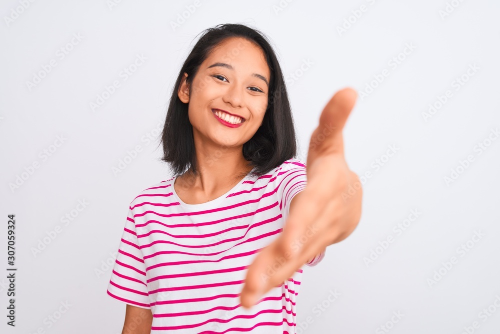 Young chinese woman wearing striped t-shirt standing over isolated white background smiling friendly offering handshake as greeting and welcoming. Successful business. Young chinese woman wearing striped t-shirt standing over isolated white background smiling friendly offering handshake as greeting and welcoming. Successful business.