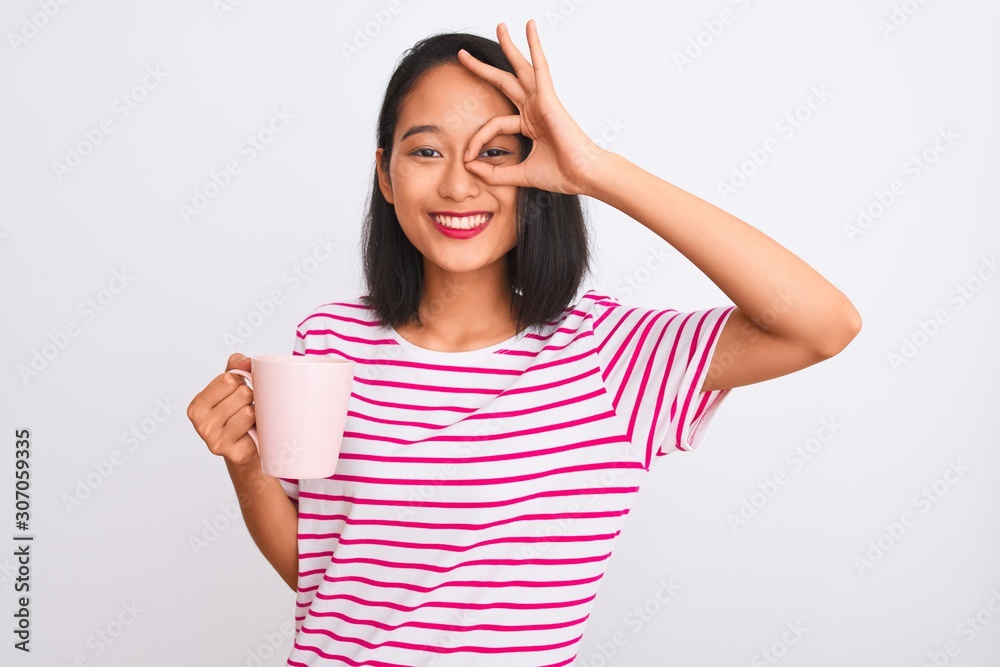 Young beautiful chinese woman drinking cup of coffee over isolated white background with happy face smiling doing ok sign with hand on eye looking through fingers Young beautiful chinese woman drinking cup of coffee over isolated white background with happy face smiling doing ok sign with hand on eye looking through fingers