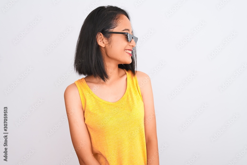 Young beautiful chinese woman wearing thug life sunglasses over isolated white background looking away to side with smile on face, natural expression. Laughing confident. Young beautiful chinese woman wearing thug life sunglasses over isolated white background looking away to side with smile on face, natural expression. Laughing confident.