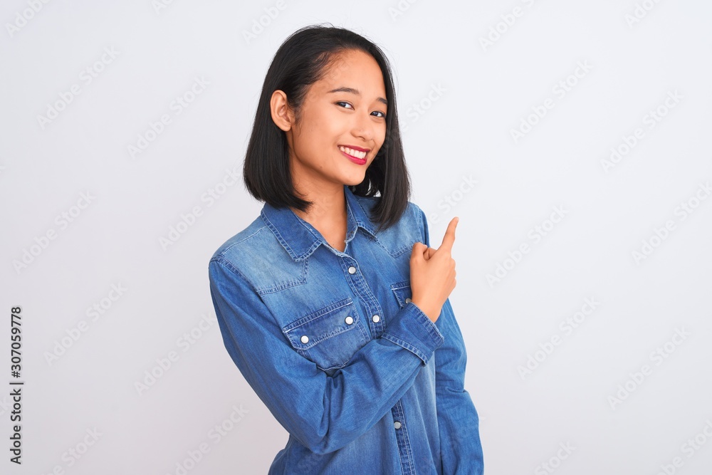 Young beautiful chinese woman wearing denim shirt standing over isolated white background cheerful with a smile of face pointing with hand and finger up to the side with happy and natural expression Young beautiful chinese woman wearing denim shirt standing over isolated white background cheerful with a smile of face pointing with hand and finger up to the side with happy and natural expression