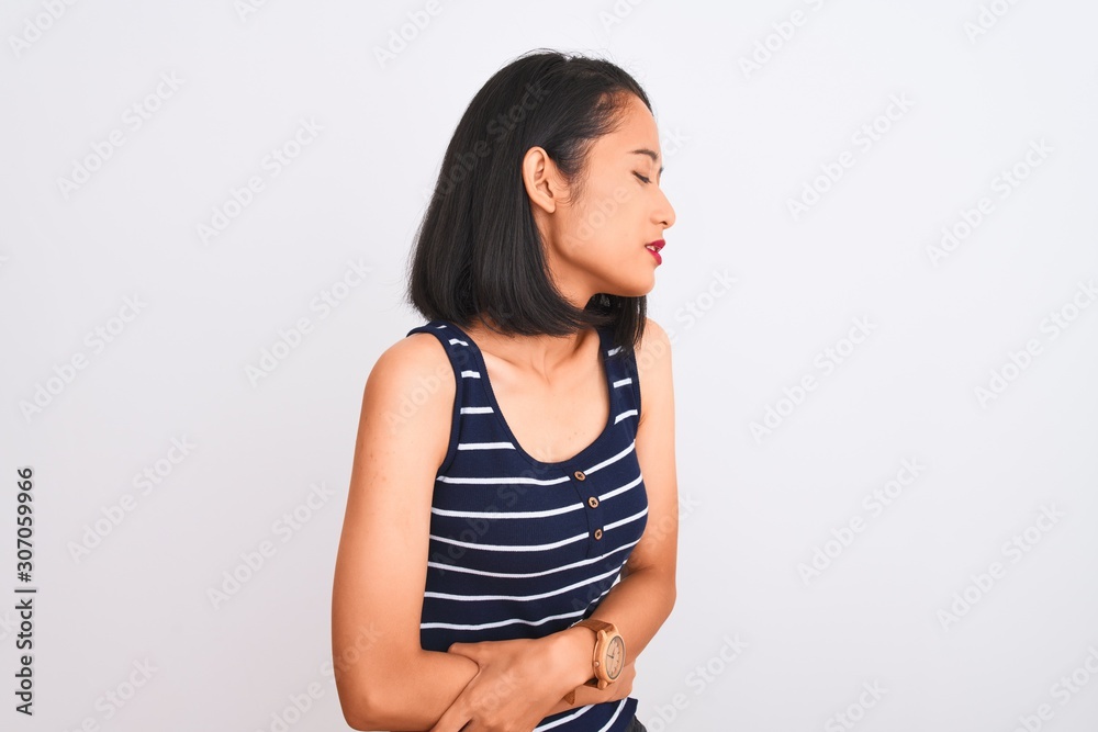 Young chinese woman wearing striped t-shirt standing over isolated white background with hand on stomach because nausea, painful disease feeling unwell. Ache concept. Young chinese woman wearing striped t-shirt standing over isolated white background with hand on stomach because nausea, painful disease feeling unwell. Ache concept.