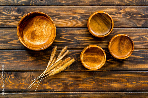Wooden bowls and ears of wheat on dark wooden background top view