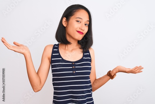 Young chinese woman wearing striped t-shirt standing over isolated white background clueless and confused expression with arms and hands raised. Doubt concept.