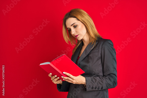 Young beautiful redhead businesswoman wearing suit reading book