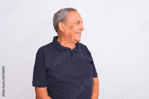 Senior grey-haired man wearing black casual polo standing over isolated white background looking away to side with smile on face, natural expression. Laughing confident.