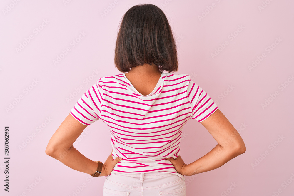 Young beautiful woman wearing striped t-shirt standing over isolated pink background standing backwards looking away with arms on body Young beautiful woman wearing striped t-shirt standing over isolated pink background standing backwards looking away with arms on body